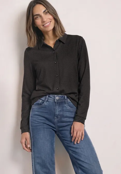 Jersey-Shirt met lange mouwen in blouse-stijl black coffee Frau trägt schwarze Bluse und blaue Jeans, steht vor neutralem Hintergrund und lächelt.