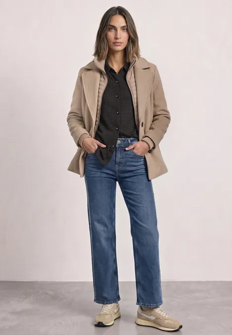 Jersey-Shirt met lange mouwen in blouse-stijl black coffee Frau in schwarzem Hemd, beige Jacke, blauen Jeans und Sneakers vor neutralem Hintergrund.