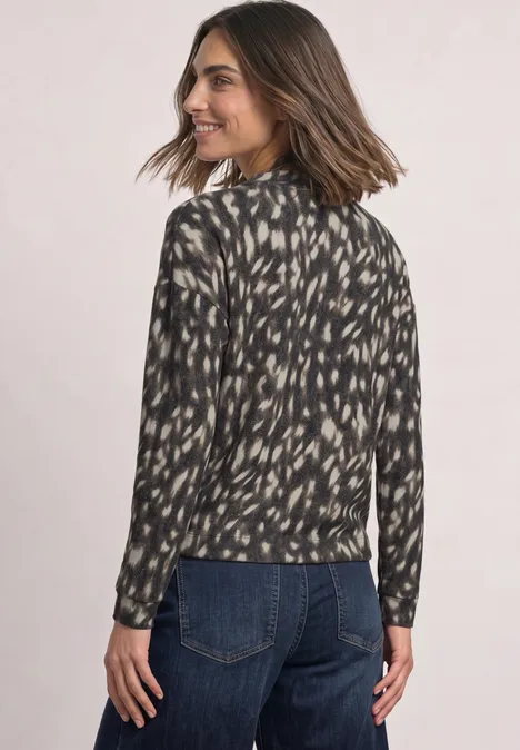 Vrouw in een zwart-beige blouse met patroon, van achteren, draait hoofd opzij en lacht.