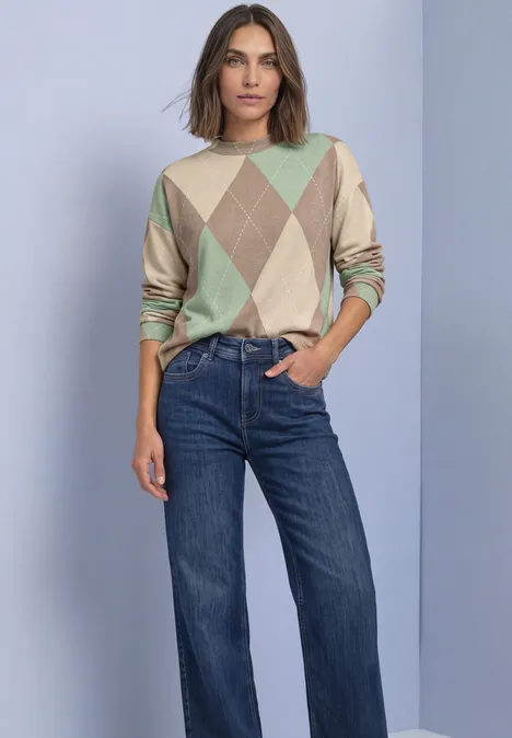 Langarm Shirt mit Turtle Neck und Muster eucalyptus green Frau in beigem und mintfarbenem Rautenmuster-Pullover und lockeren Jeans vor neutralem Hintergrund.