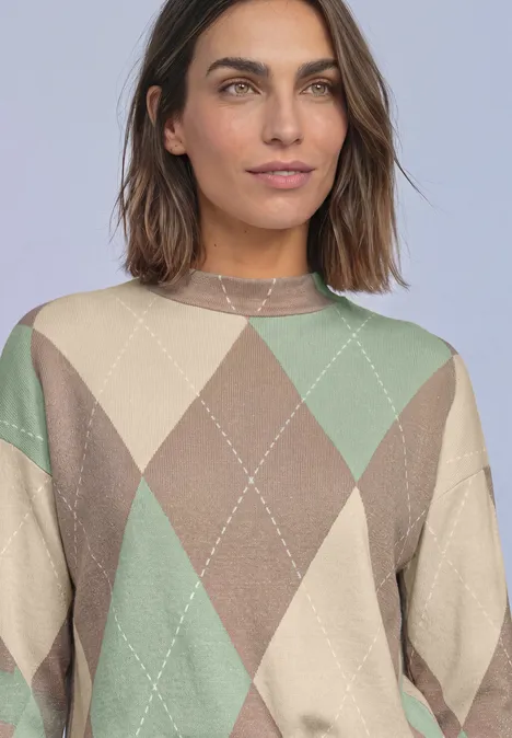 Langarm Shirt mit Turtle Neck und Muster eucalyptus green Frau mit schulterlangem braunem Haar und beigem Pullover mit Argyle-Muster vor neutralem Hintergrund.