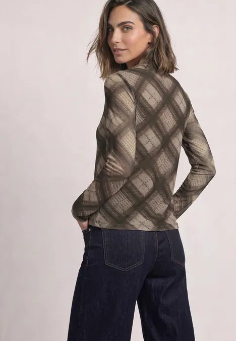 Een vrouw in een bruin geruit coltrui en donker denim, kijkt over haar schouder.