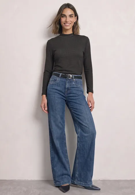 3/4-Arm Shirt mit Turtle Neck und Print black coffee Frau in schwarzem Langarmshirt und weitem Jeans, steht lässig vor hellem Hintergrund.