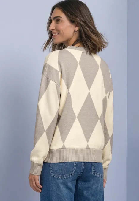 Vrouw van achteren in een beige-crèmekleurige gebreide trui met ruitpatroon en blauwe spijkerbroek.