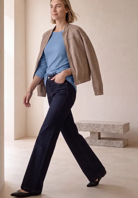Basic Shirt mit U-Boot-Ausschnitt northern blue Frau im blauen Top und weiten Jeans mit hellbrauner Jacke über den Schultern vor minimalistischem Hintergrund