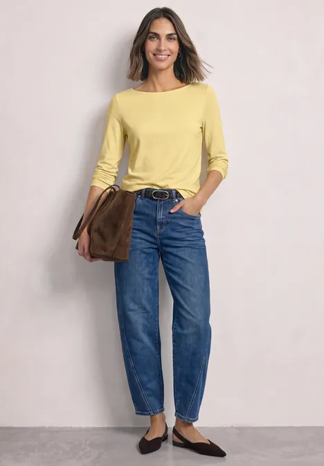 Basic Shirt mit U-Boot-Ausschnitt sunbeam yellow Frau in gelbem Langarmshirt, lockeren Jeans und flachen Schuhen hält eine braune Tasche lässig über der Schulter.