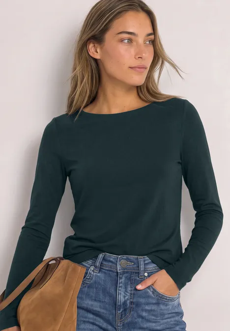 Junge Frau mit dunkelgrünem Langarmshirt und Jeans, trägt eine braune Schultertasche.
