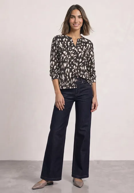 Langarm Shirt im Tunika-Look Black Eine Frau trägt eine schwarz-weiße, gemusterte Bluse, weite, dunkelblaue Jeans und schwarze Schuhe.