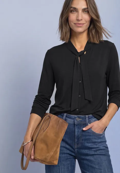 Langarm Shirt im Blusen-Look Black Frau trägt schwarze Bluse mit neckholder-Knoten, blaue Jeans und eine braune Wildledertasche.