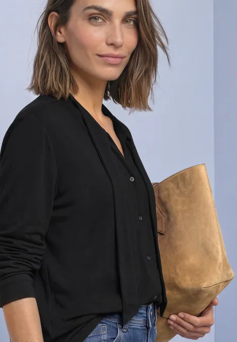 Langarm Shirt im Blusen-Look Black Frau mit schulterlangem braunem Haar in schwarzem Cardigan, die eine beige Clutch hält.