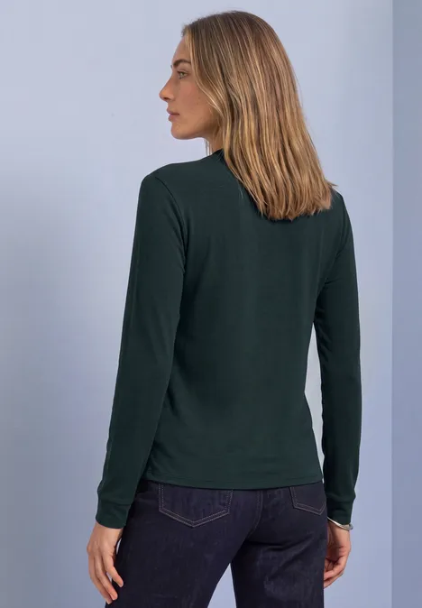Shirt met lange mouwen in blouse-stijl stormy green Vrouw van achteren in een donkergroen shirt met lange mouwen en een spijkerbroek voor een neutrale achtergrond.