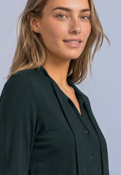 Shirt met lange mouwen in blouse-stijl stormy green Portret van een glimlachende vrouw met lichte ogen en een zwarte blouse voor een lichte achtergrond.