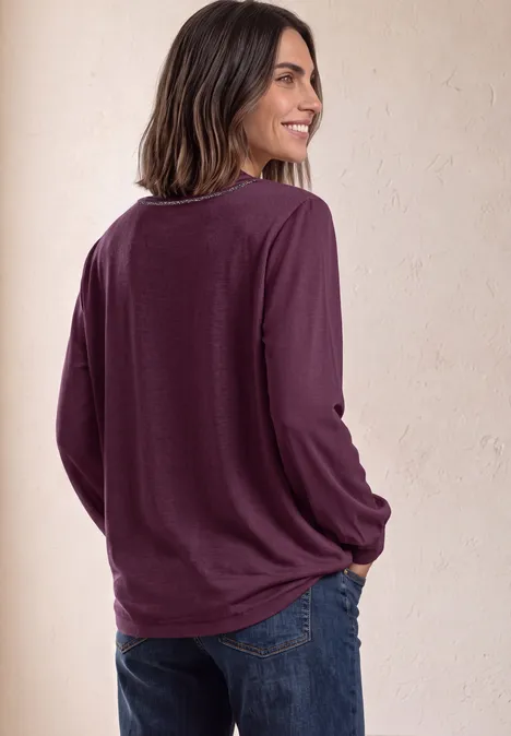 2-in-1 Sirt aus Chiffon mit Boat Neck berry maroon Eine Frau trägt ein langärmeliges, dunkelviolettes Shirt und blaue Jeans, sie steht seitlich zum Betrachter.