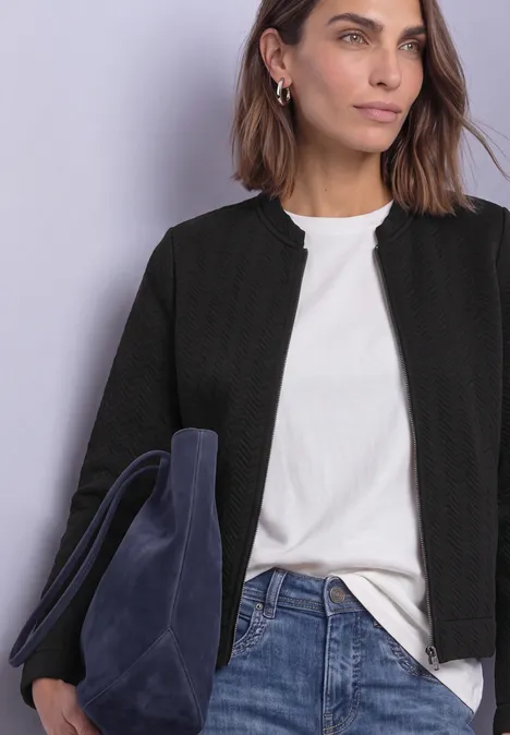 Leichte Sweatjacke mit Struktur und Zipper Black Frau mit schwarzer Jacke, weißem T-Shirt und Jeans hält eine dunkelblaue Wildledertasche.