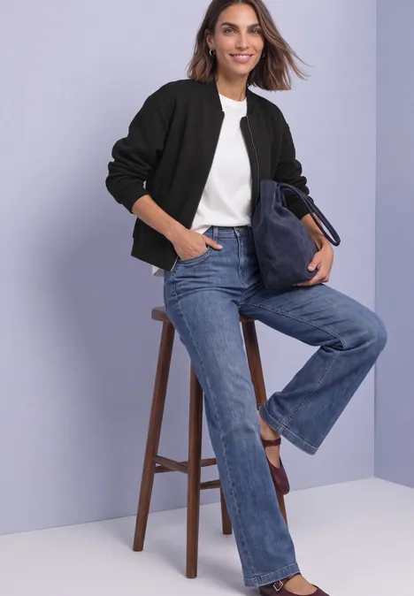 Leichte Sweatjacke mit Struktur und Zipper Black Frau sitzt auf Hocker, trägt Jeans, weißes T-Shirt und schwarzen Blouson, lächelt.