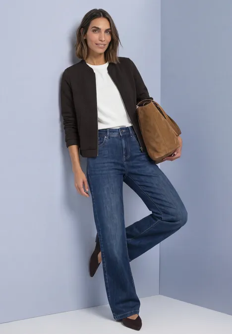 Leichte Sweatjacke mit Struktur und Zipper black coffee Frau in weißem T-Shirt, schwarzer Strickjacke, weitem Jeans und brauner Tasche vor blauem Hintergrund.