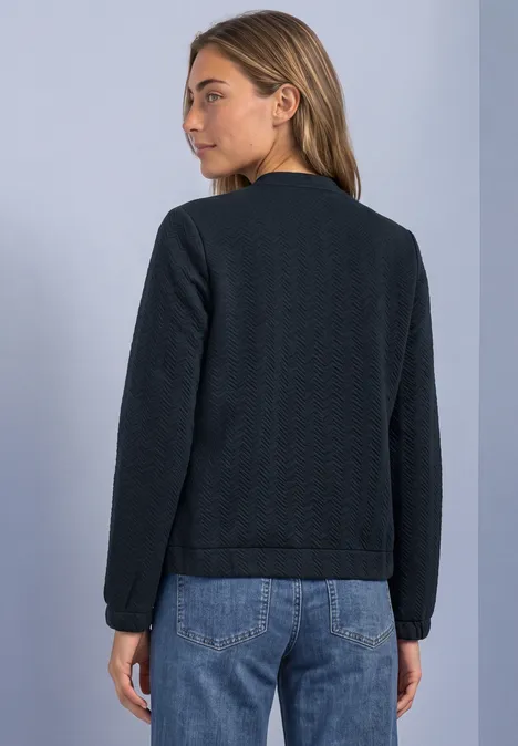 Leichte Sweatjacke mit Struktur und Zipper darkest blue Frau von hinten in schwarzer, leichter gesteppter Jacke und blauen Jeans vor hellem Hintergrund.