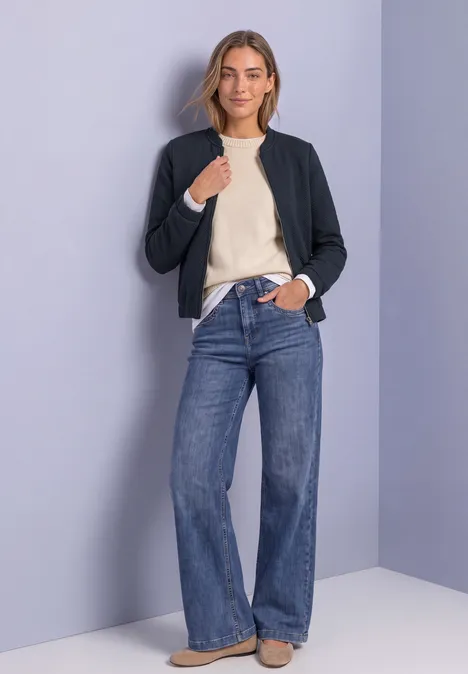 Leichte Sweatjacke mit Struktur und Zipper darkest blue Frau in schwarzer Bomberjacke, hellem Pulli und weiten Jeans vor lila Hintergrund.