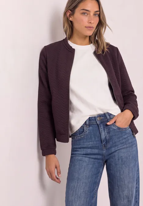 Leichte Sweatjacke mit Struktur und Zipper berry plum Frau in weißem T-Shirt, violetter Bomberjacke und blauen Jeans vor neutralem Hintergrund.