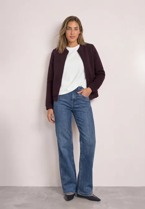 Leichte Sweatjacke mit Struktur und Zipper berry plum Frau mit weißem Shirt, bordeauxfarbener Jacke und weiten Jeans vor neutralem Hintergrund.