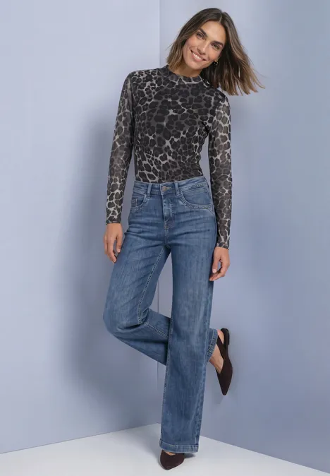 Frau in grauem Leo-Print-Body und weiten High-Waist-Jeans, die lächelnd vor neutralem Hintergrund posiert.