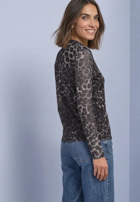 Frau in langärmeligem Shirt mit Leopardenmuster und Jeans vor violettem Hintergrund.