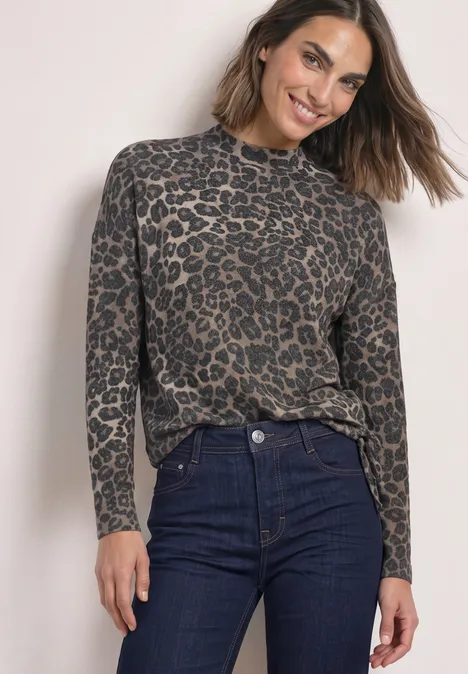Langarm Shirt mit Turtle neck und Leo-Muster Black Frau trägt Leo-Muster-Pullover und dunkle Jeans, lächelnd vor hellem Hintergrund.