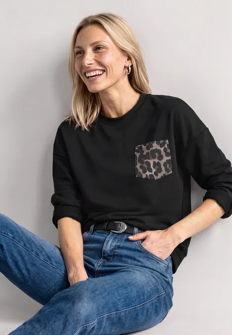 Lachende vrouw in zwart shirt met luipaardzakje en blauwe spijkerbroek.