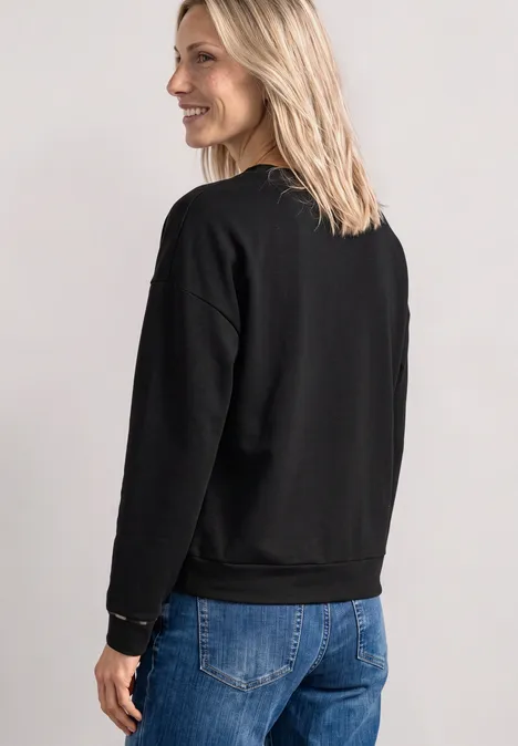 Vrouw in profiel met zwarte trui en blauwe jeans.