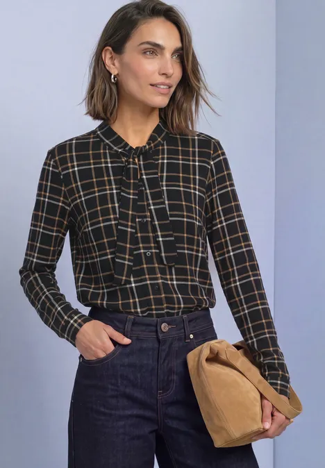 Langarm Shirt im Blusen-Look mit Karomuster Black Frau in karierter Bluse mit Schleifenkragen, Jeans und samtfarbener Clutch.