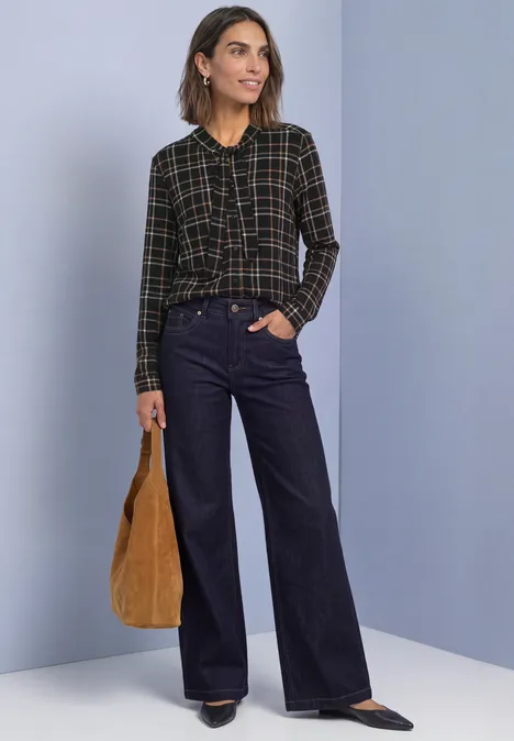 Langarm Shirt im Blusen-Look mit Karomuster Black Frau in kariertem Hemd und weiten Jeans steht vor einfarbiger Wand, hält braune Tasche.