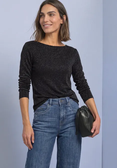 Shirt met lange mouwen, boothals en glitters Black Frau trägt schwarzen Pullover, blaue Jeans und hält eine schwarze Clutch. Steht vor hellem Hintergrund.