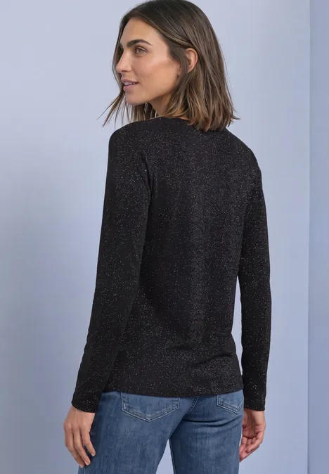 Shirt met lange mouwen, boothals en glitters Black Frau im schwarzen Langarmpullover und Jeans steht mit dem Rücken zur Kamera und schaut über die Schulter.