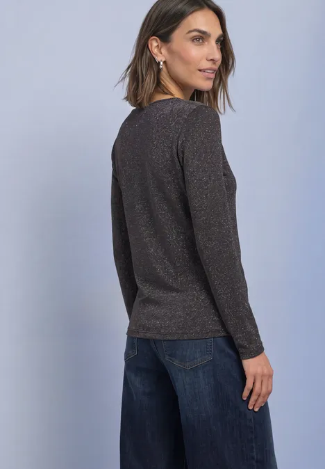 Langarm Shirt mit Boat Neck und Glitzer black coffee Eine Frau steht mit dem Rücken zur Kamera und schaut über die Schulter, sie trägt einen dunkelglänzenden Pullover und Jeans.