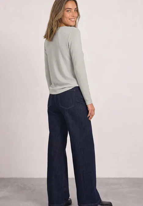 T-shirt à manches longues, col bateau et paillettes pure beige Lächelnde Frau im hellgrauen Langarmshirt und weiten, dunklen Jeans, schaut über die Schulter.