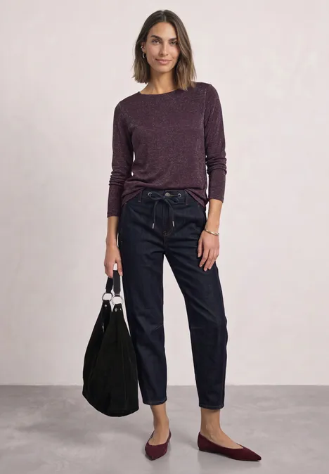 Langarm Shirt mit Boat Neck und Glitzer berry plum Frau trägt lila Pullover, hohe Jeans und burgunderfarbene Ballerinas, hält schwarze Tasche.