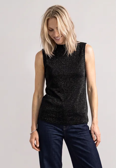 Eine Frau trägt ein schwarzes Glitzer-Top und blaue Jeans.