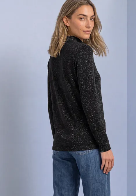 Shirt met lange mouwen, col en glitters Black Vrouw in zwarte glittertrui en blauwe spijkerbroek kijkt over haar schouder.
