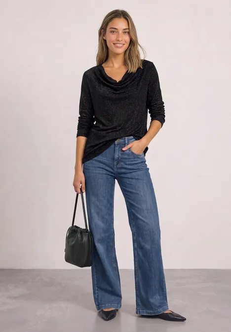 Langarm Shirt mit Wasserfallfront Black Frau in schwarzem Wasserfall-Pulli, weiten blauen Jeans, spitzen Flats und schwarzer Ledertasche.