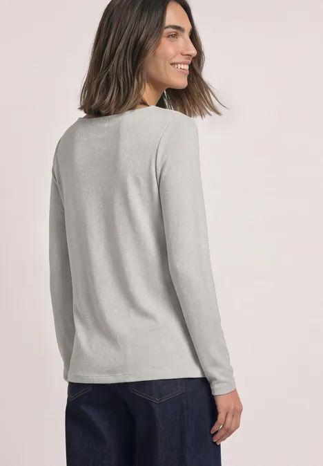 T-shirt à manches longues avec encolure en cascade pure beige Frau leicht seitlich von hinten, lächelt, trägt graues Langarmshirt und Jeans