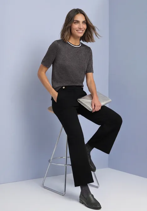 Kurzarm Shirt mit Rundhals und Glitzer black coffee Frau in grauem Shirt und schwarzen Hosen sitzt auf einem Hocker, hält eine Clutch und trägt Stiefeletten.