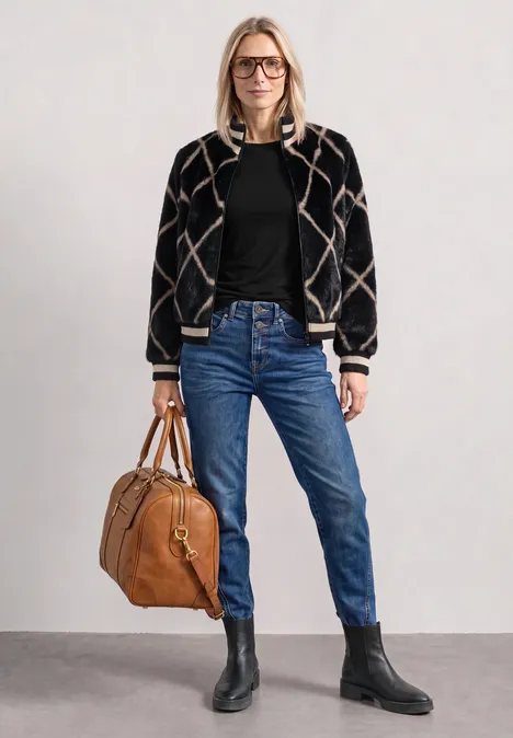 Basic shirt met boothals Black Frau mit gemusterter Bomberjacke, schwarzem Pullover, blauen Jeans und schwarzen Stiefeln, trägt eine braune Ledertasche.