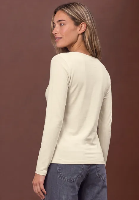 Femme vue de dos portant un haut à manches longues crème et un jean bleu sur fond marron.