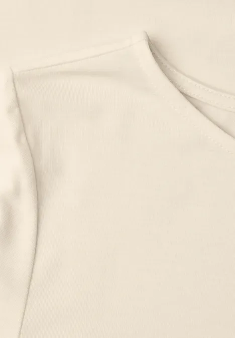 Gros plan d’un t-shirt beige clair en coton avec col rond et manche courte.