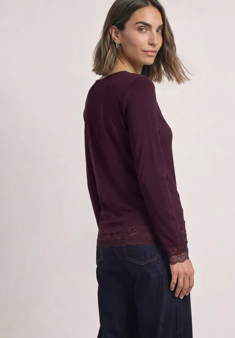 Shirt met lange mouwen, boothals en kant berry plum Vrouw in profiel met een donkerpaarse trui met lange mouwen en donkerblauwe jeans.
