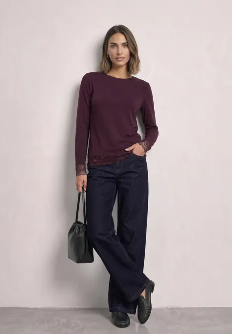 Shirt met lange mouwen, boothals en kant berry plum Een vrouw draagt een bordeaux trui, donkere wijde broek en houdt een zwarte tas vast.