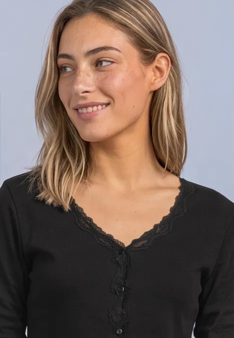 Jasje met fijne ribbel, V-hals en kant Black Jonge vrouw met blond haar in een zwart kanten topje, glimlachend en zijwaarts kijkend.