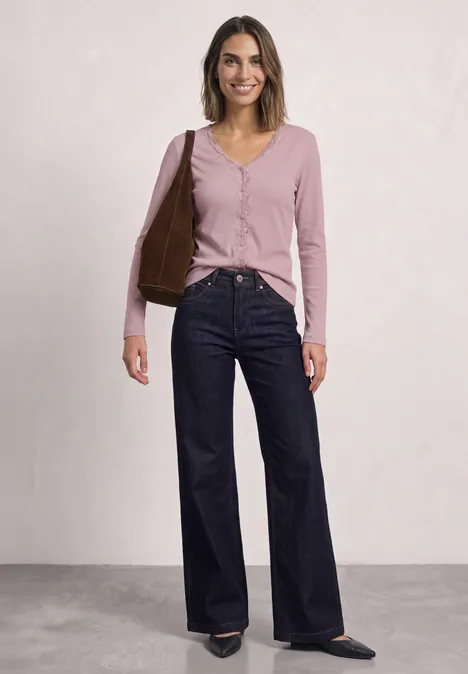 Jasje met fijne ribbel, V-hals en kant quiet rose Frau trägt rosa Cardigan, dunkelblaue Schlagjeans und hält eine braune Tasche.