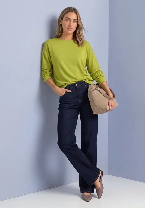Shirt met gebreide look en vleermuismouwen apple lime Vrouw in felgroene trui, donkerblauwe jeans en beige tas, staand voor een lichte achtergrond.