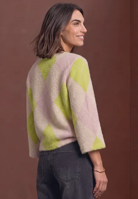 Seitliche Aufnahme einer Frau in rosa-limettenfarbigem Rautenpullover und schwarzer Jeans vor braunem Hintergrund